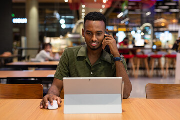 Portrait of handsome young black man using laptop computer in coffee shop