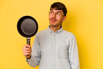 Young hispanic cooker holding frying pan isolated on yellow background dreaming of achieving goals and purposes