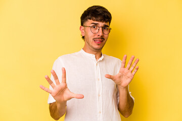 Young caucasian man isolated on yellow background rejecting someone showing a gesture of disgust.