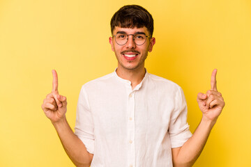 Young caucasian man isolated on yellow background indicates with both fore fingers up showing a...