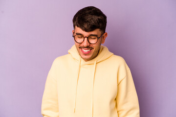 Young caucasian man isolated on purple background laughs and closes eyes, feels relaxed and happy.