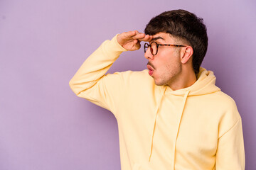 Young caucasian man isolated on purple background looking far away keeping hand on forehead.