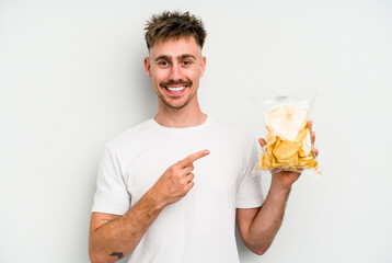 Young caucasian man holding crisps isolated on white background smiling and pointing aside, showing something at blank space.