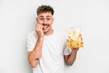 Young caucasian man holding crisps isolated on white background biting fingernails, nervous and very anxious.