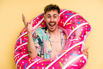 Young caucasian man holding an inflatable donut isolated on yellow background receiving a pleasant...