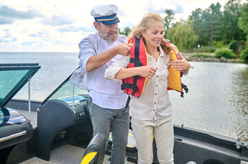 A man in helping a blonde woman to put on the life vest