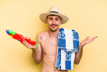 Young caucasian man holding water gun isolated on yellow background