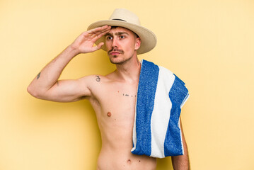 Young caucasian man holding a towel isolated on yellow background