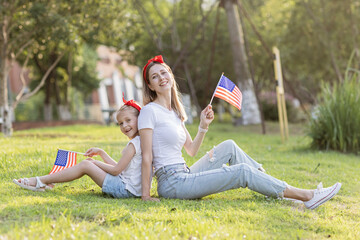 Patriotic holiday. Happy family, mother and daughter with American flag outdoors on sunset. USA...