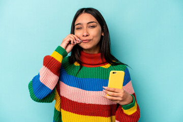Young caucasian woman holding mobile phone isolated on blue background with fingers on lips keeping a secret.