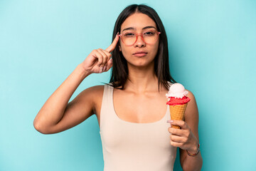 Young hispanic woman holding an ice cream isolated on blue background pointing temple with finger, thinking, focused on a task.