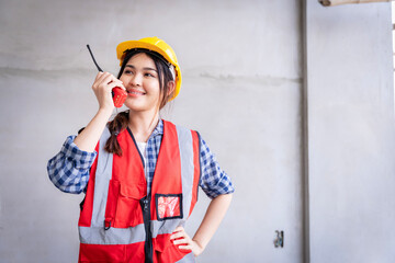 Portrait of an Asian woman civil engineer wearing a red reflective jacket. Wear a yellow helmet against the backdrop of a wall under construction.