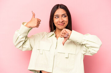 Young hispanic woman isolated on pink background showing thumbs up and thumbs down, difficult...