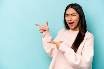 Young hispanic woman isolated on blue background pointing with forefingers to a copy space, expressing excitement and desire.