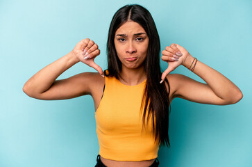 Young hispanic woman isolated on blue background showing a dislike gesture, thumbs down....