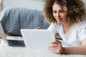 smiling woman using digital tablet on floor near laptop.