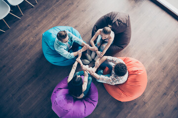 Top angle view photo of positive good mood workers group sitting dorm beanbags arms folded indoors...