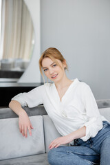 Portrait of smiling blonde woman sitting on couch.