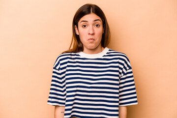 Young hispanic woman isolated on beige background shrugs shoulders and open eyes confused.