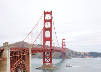 Golden Gate Bridge on a clear day, clouds blowing through the sky. Red ship in water under the bridge. - Powered by Adobe