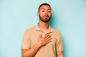 Young hispanic man isolated on blue background taking an oath, putting hand on chest.