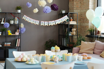 Horizontal image of living room decorating with poster and balloons for birthday party with candy bar on table
