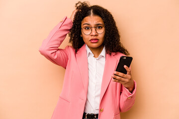 Young African American woman holding mobile phone isolated on beige background being shocked, she...