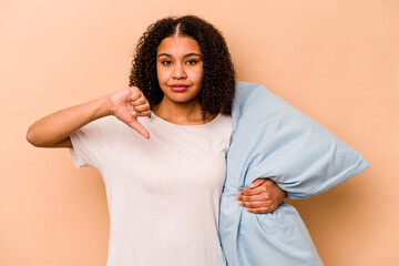 Young African American woman holding a pillow isolated on beige background showing a dislike...