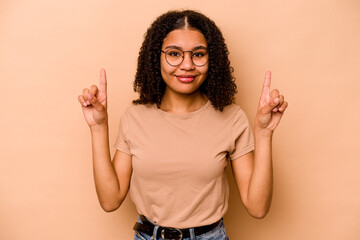 Young African American woman isolated on beige background indicates with both fore fingers up...