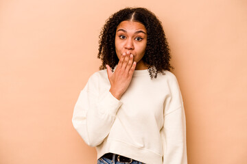 Young African American woman isolated on beige background shocked, covering mouth with hands, anxious to discover something new.