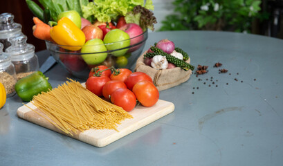 Bunch of Italian spaghetti raw closeup with tomatoes and vegetables, herb on a rustic kitchen on a wooden table.