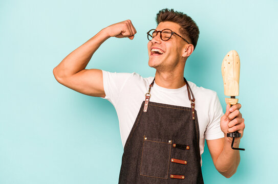 Young caucasian shoemaker isolated on blue background raising fist after a victory, winner concept.