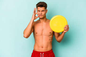 Young caucasian man playing with frisky isolated on blue background with fingers on lips keeping a...