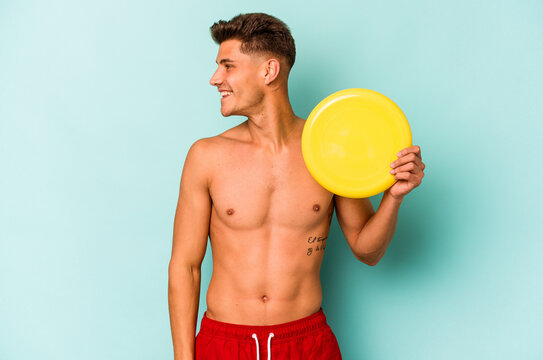 Young caucasian man playing with frisky isolated on blue background looks aside smiling, cheerful and pleasant.