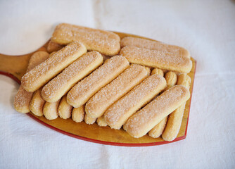 Top view of ladyfinger savoiardi biscuit cookies on a wooden cutting board on white tablecloth background. Close up