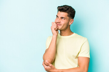 Young caucasian man isolated on blue background relaxed thinking about something looking at a copy space.