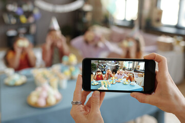 Close-up of woman taking photo of group of children on mobile phone while they sitting at table and fooling around