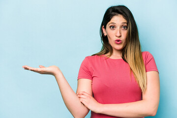 Fototapeta premium Young caucasian woman isolated on blue background impressed holding copy space on palm.