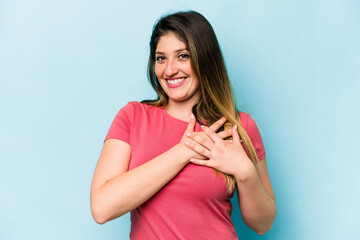 Young caucasian woman isolated on blue background has friendly expression, pressing palm to chest. Love concept.