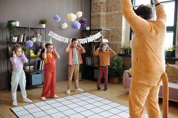 Group of children playing and dancing with animator in animal costume during birthday party at home