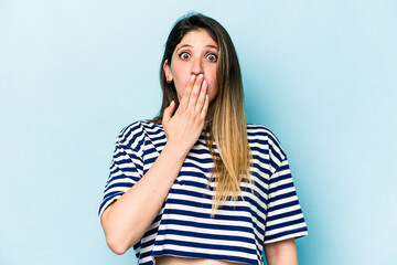 Young caucasian woman isolated on blue background shocked, covering mouth with hands, anxious to discover something new.