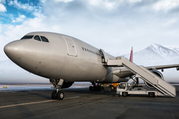 Fototapeta na wymiar Wide body passenger airplane and aircraft steps at the airport apron on the background of high scenic snow-capped mountains