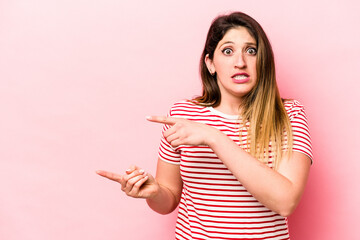 Young caucasian woman isolated on pink background shocked pointing with index fingers to a copy space.