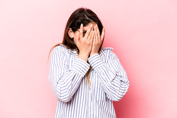 Young caucasian woman isolated on pink background blink at the camera through fingers, embarrassed covering face.