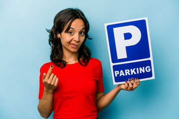 Young hispanic woman holding parking placard isolated on blue background pointing with finger at you as if inviting come closer.