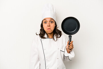 Young hispanic chef woman isolated on white background shrugs shoulders and open eyes confused.