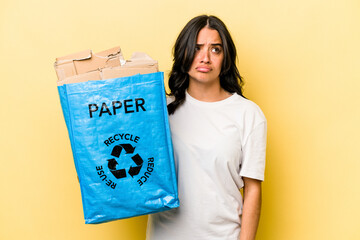 Young hispanic woman recycling paper isolated on yellow background confused, feels doubtful and unsure.