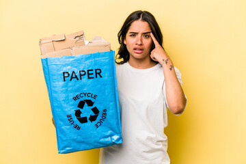 Young hispanic woman recycling paper isolated on yellow background showing a disappointment gesture with forefinger.