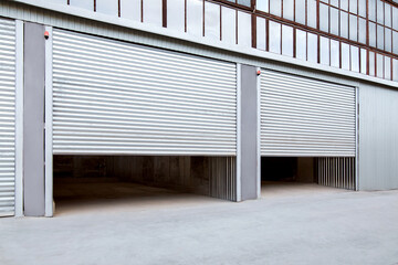Opening gray iron shutter door of garage and industrial building warehouse exterior facade with grey concrete road, side view nobody.