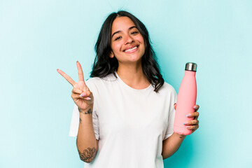 Young hispanic woman holding thermo isolated on blue background joyful and carefree showing a peace...